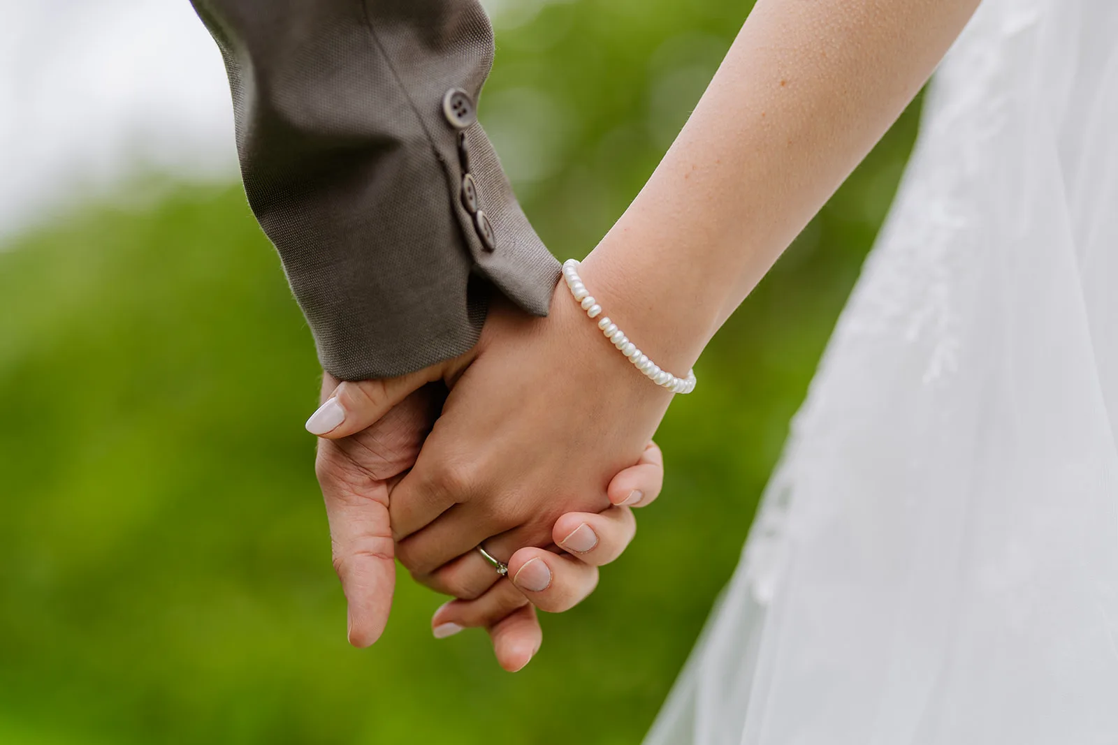 Hände haltendes Brautpaar mit Perlenarmband, Nahaufnahme bei der Hochzeit auf dem Bächlihof in Jona
